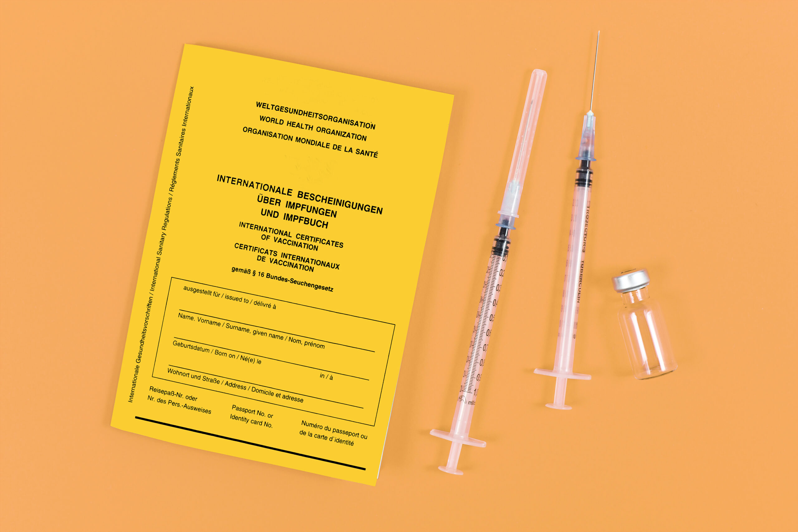 Yellow certificate of vaccination next to syringes and vial on orange background
