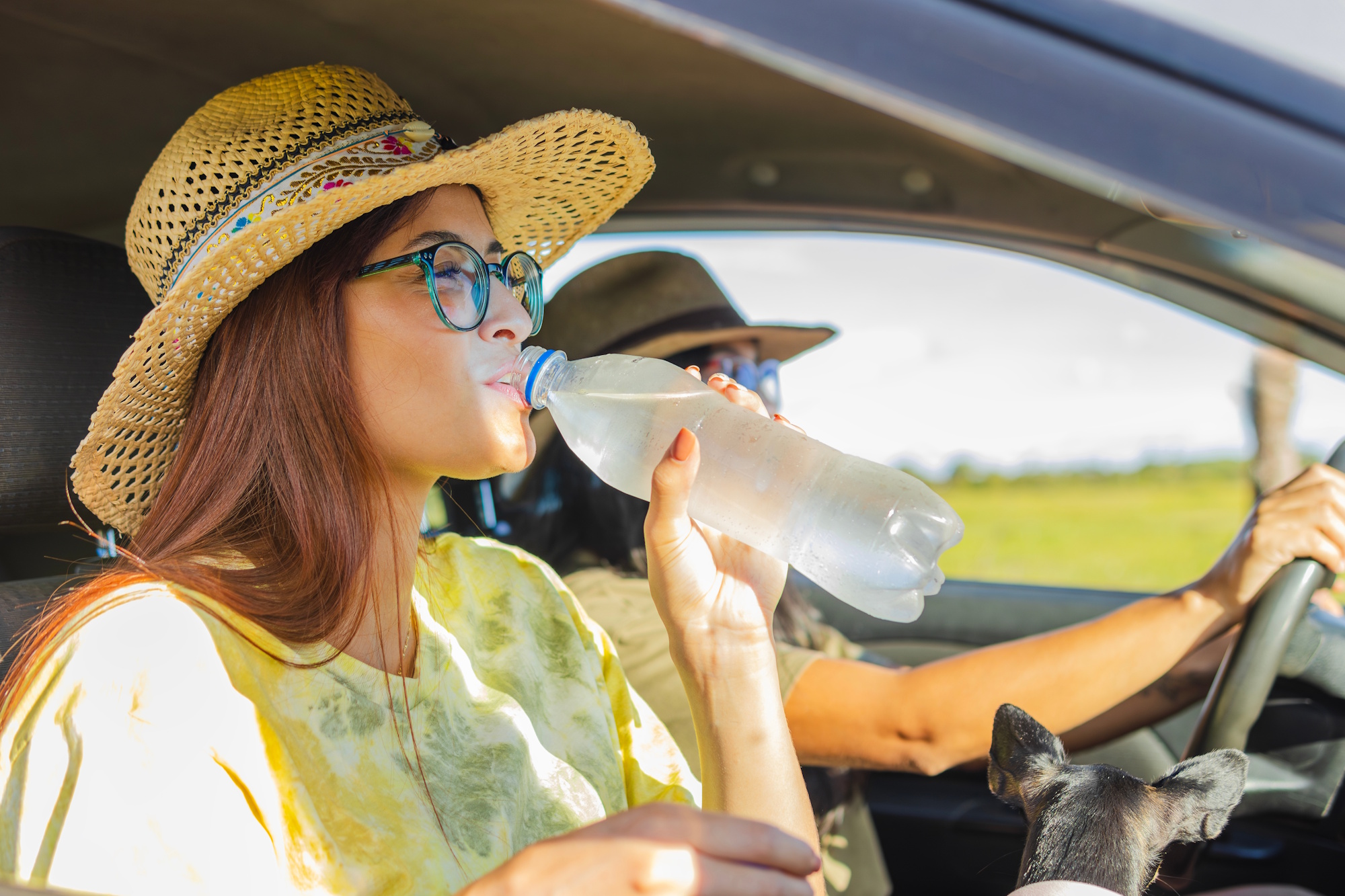 woman in car wearing hat drinking water
