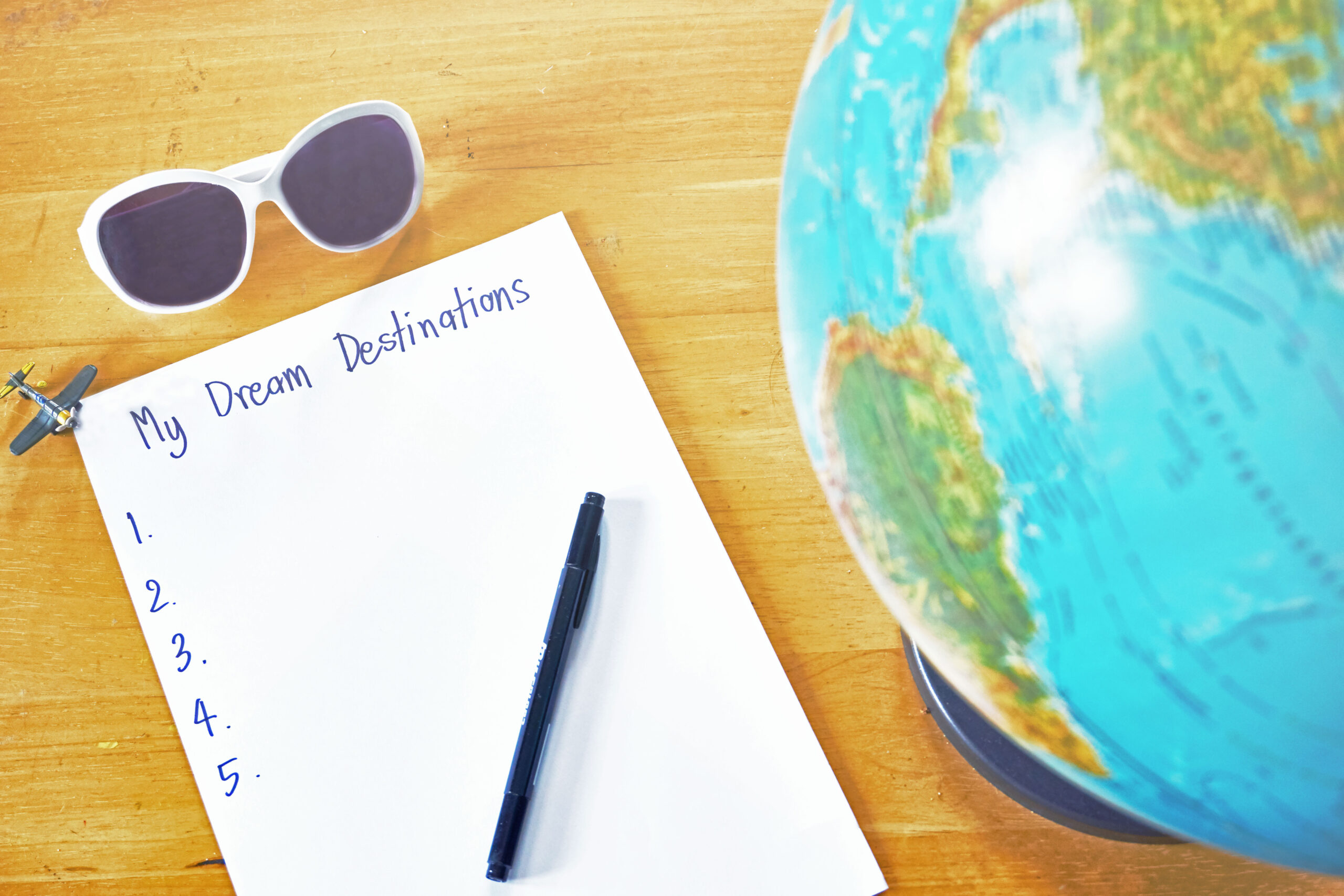 Dream destination list on the paper with pen and world globe map on wooden table