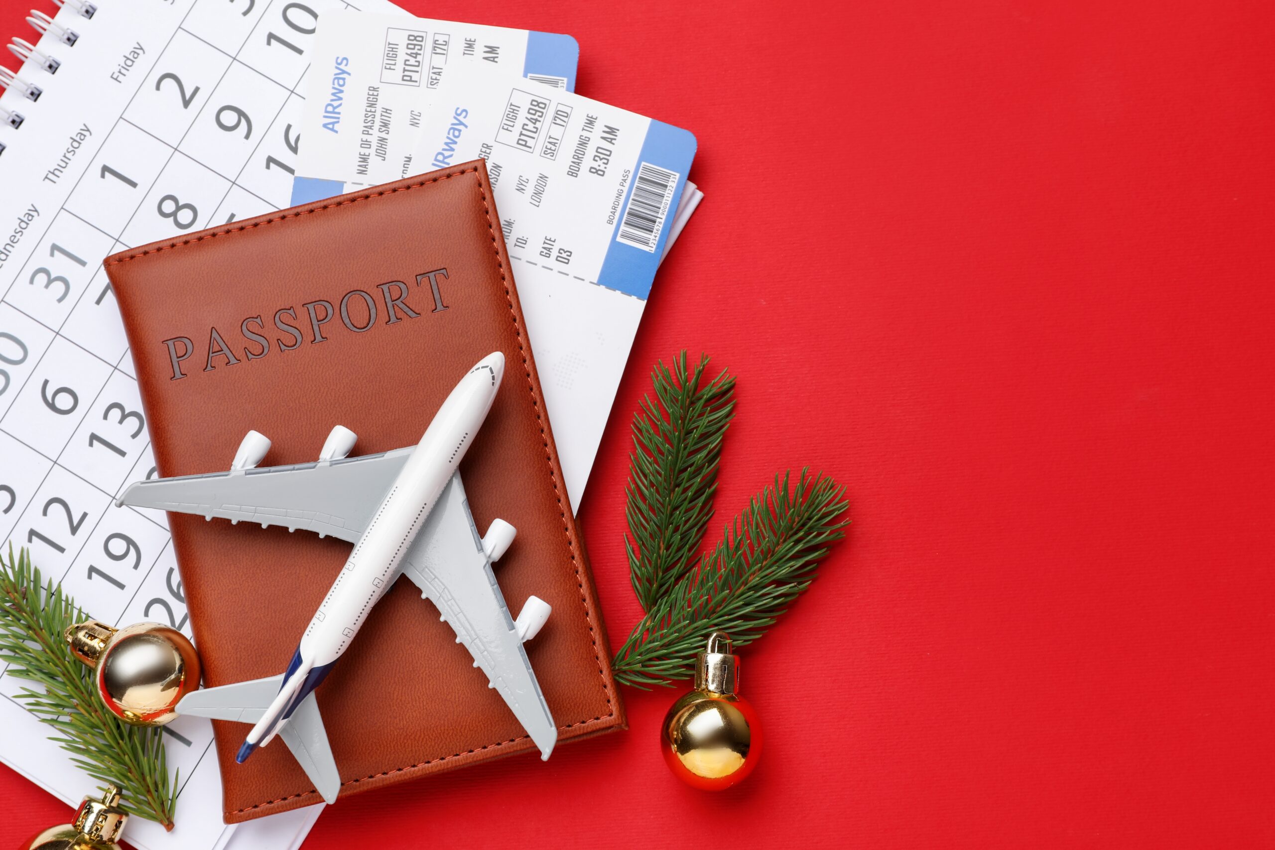 Christmas vacation. Passport with tickets, toy plane, calendar, fir branches and baubles on red background