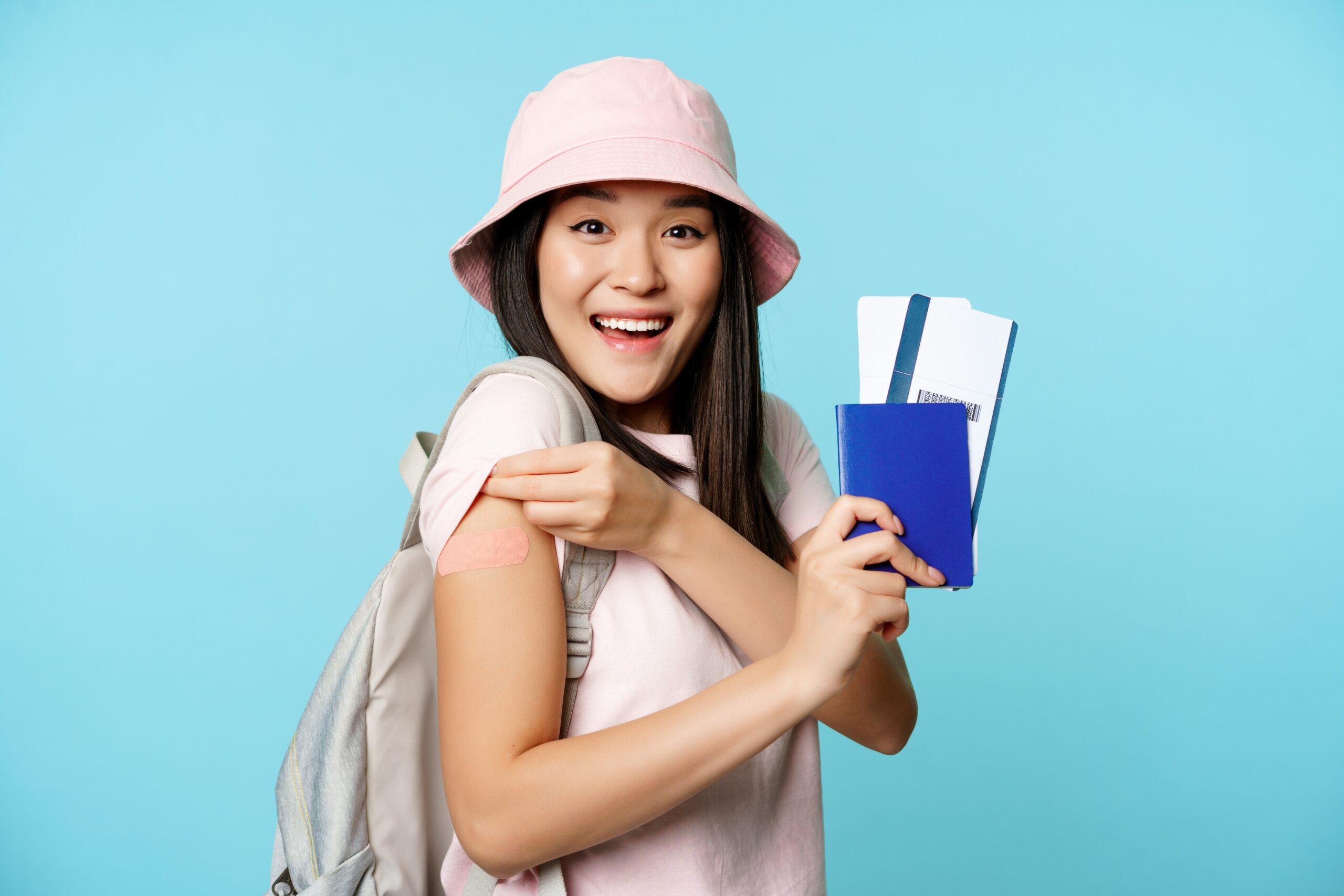 Enthusiastic female tourist shows her vaccinated arm, passport and plane tickets.