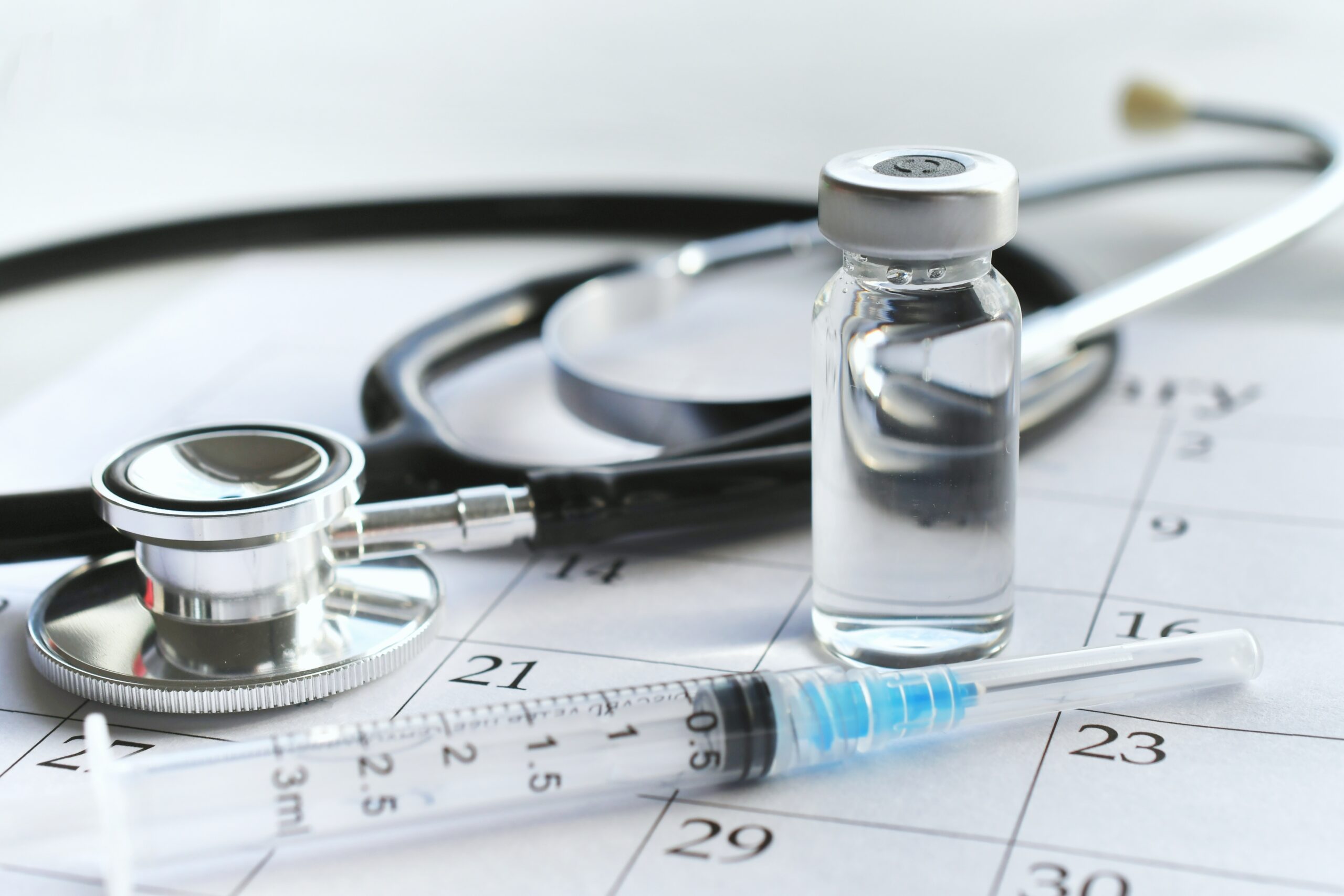 Medical syringe laying on calendar page with a stethoscope