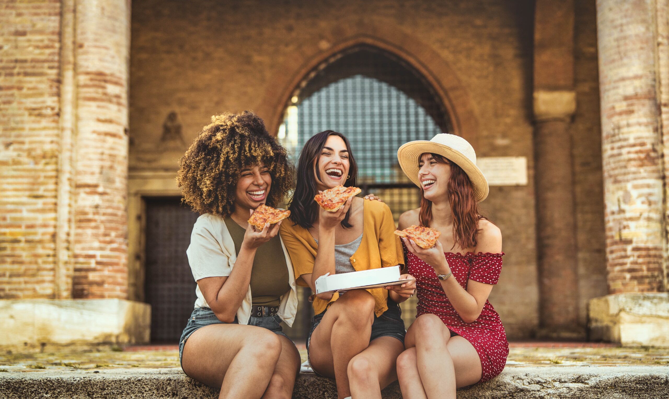 Three young female friends eating street food in the city