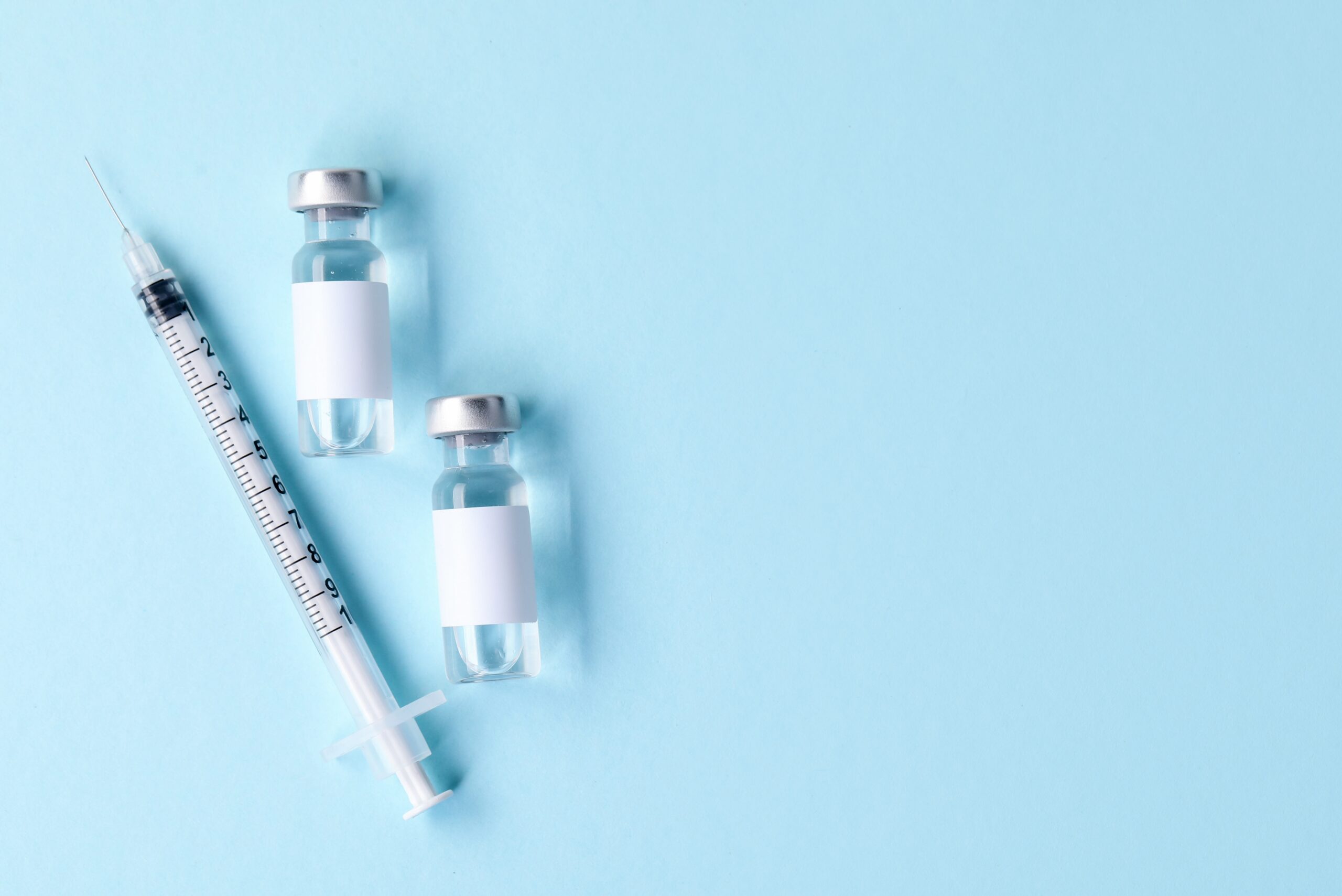 Vaccine in vials and syringe on light blue background