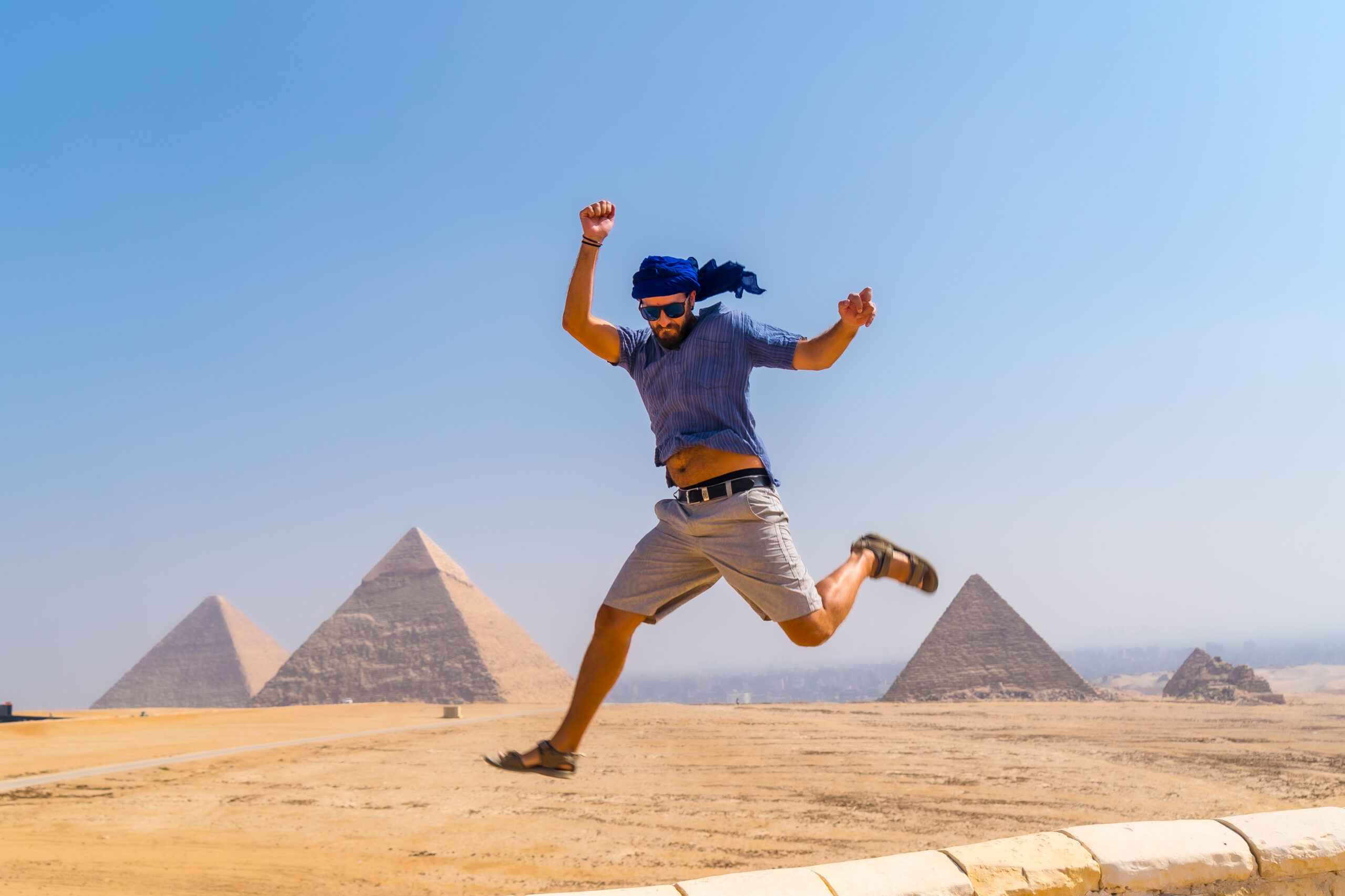Male tourist jumping for joy in a blue turban and sunglasses in front The Pyramids of Giza Male tourist jumping for joy in a blue turban and sunglasses in front The Pyramids of Giza